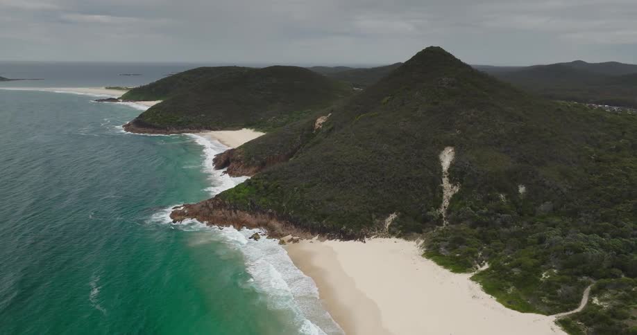 Aerial view of an empty beach with green sea surrounded by hills covered with trees