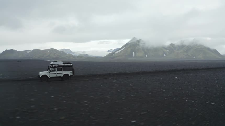 A jeep driving on a dirt road in a natural setting with snowcapped mountains in the distance on a cloudy day