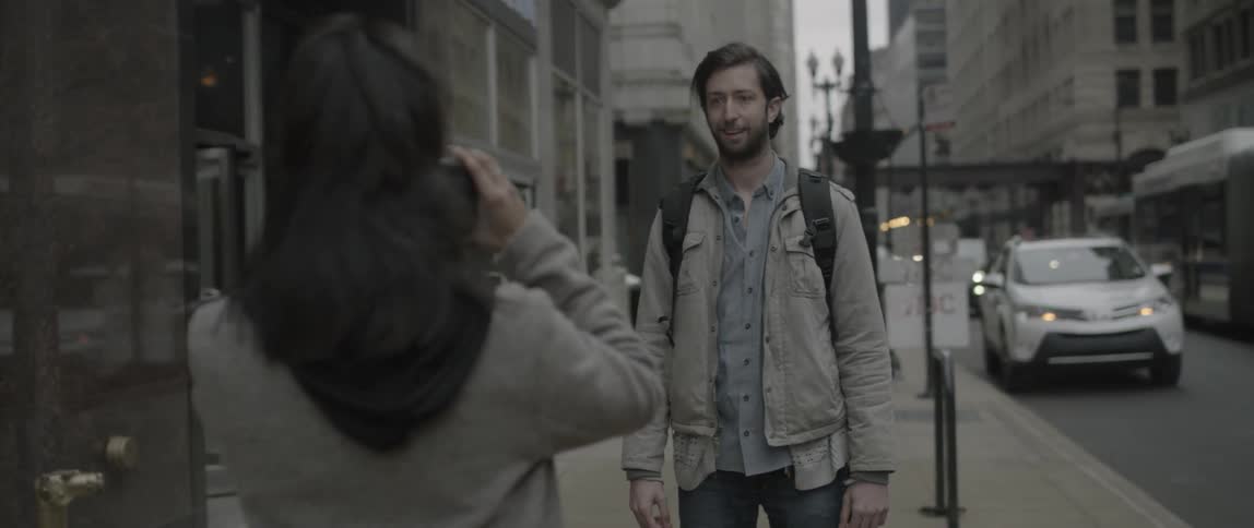 A woman takes a photograph of a man on a city street
