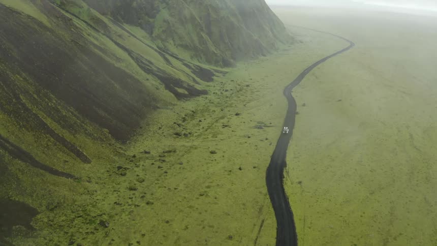 Aerial of a car driving along a road in a landscape with green mountains