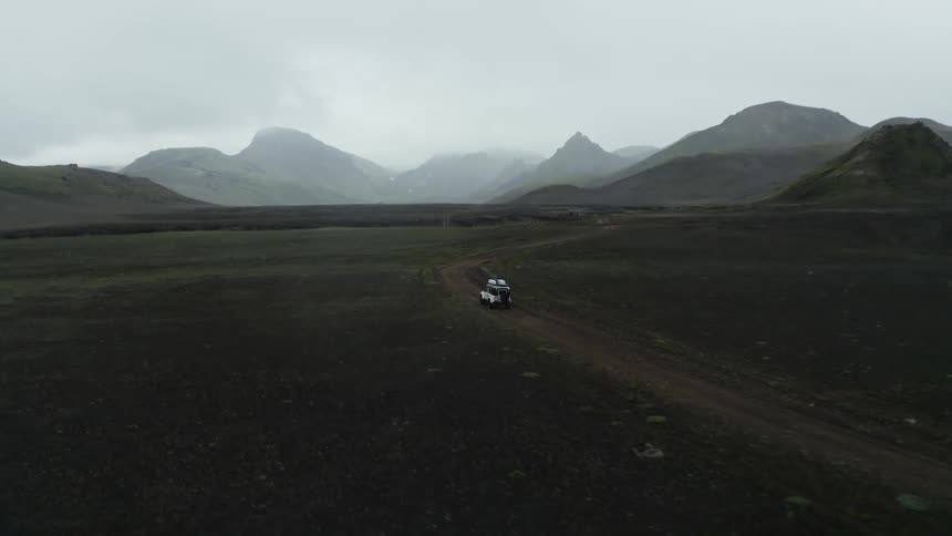 Jeep driving on a dirt road amidst a mountain range on a cloudy day with thick haze
