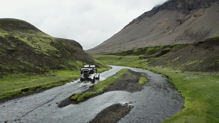 A car driving along the small river in the landscape with rocky mountains