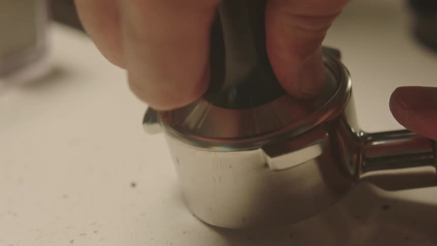Closeup of a handle with coffee being tamped and leveled uniformly