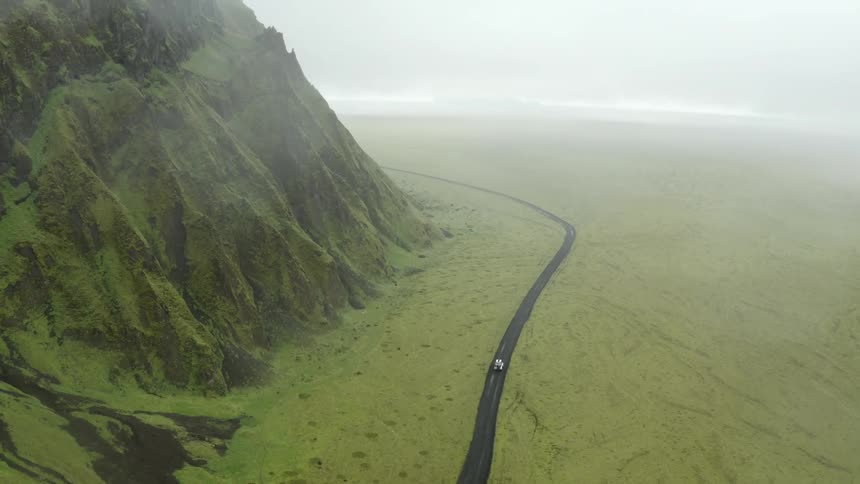 Aerial view of a car driving on a road through green fields and mountains