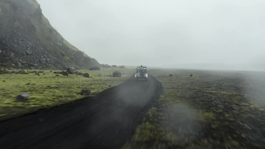 A jeep riding on a road next to a mountain with a foggy atmosphere