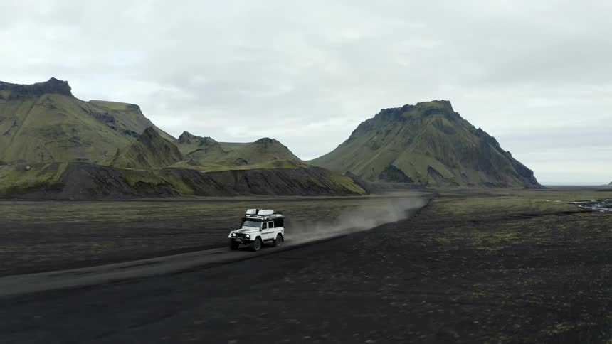 Jeep driving on the ground next to mountains on a cloudy day