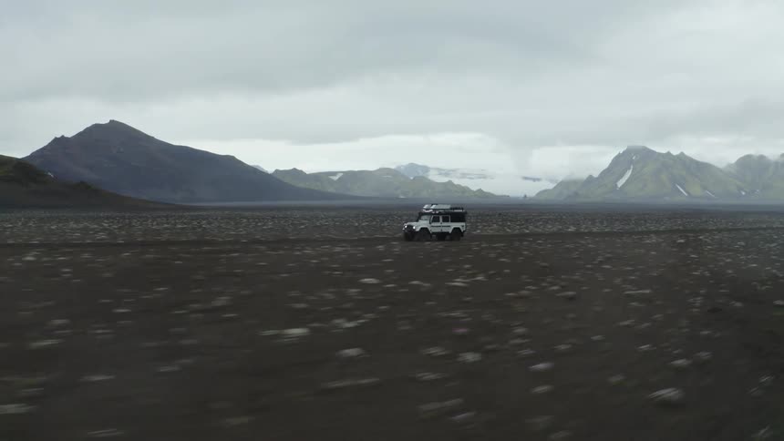 Jeep driving on the ground next to a mountain range on a cloudy day