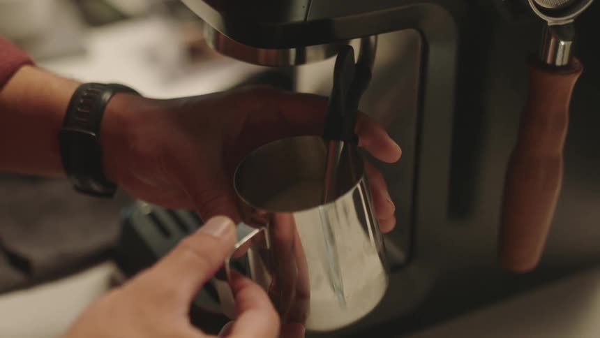 Closeup of a persons hands pouring milk into a cappuccino through a machine