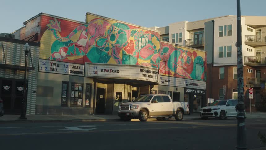 A theater with a drawing on top and some cars parked in front