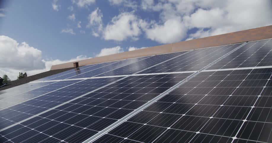 Passing clouds reflect on solar panels on a building