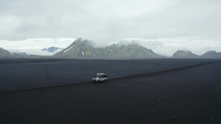 A car driving along the dirt road in the landscape of plains and mountains