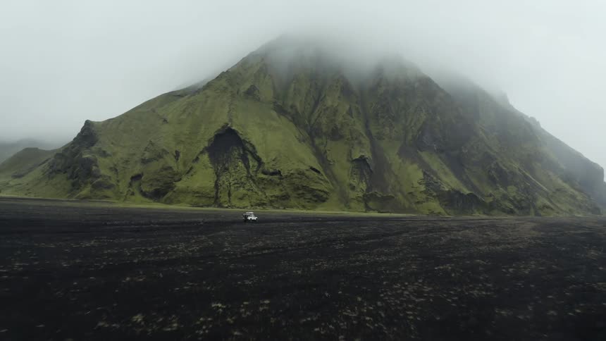 Jeep driving on a dirt road beside mountains under a hazy sky and weather