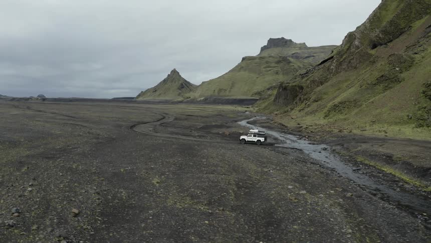 Jeep driving under the river and dirt road alongside mountains