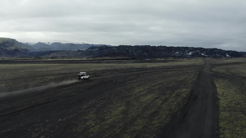 Aerial of white jeep driving on dirt road in the desert on a cloudy day