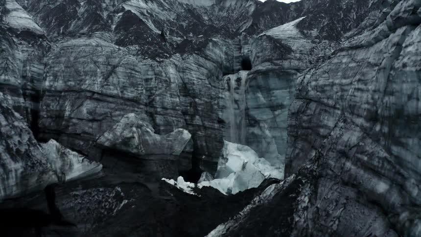A waterfall cascades down a rocky gray cliff onto snow and ice below