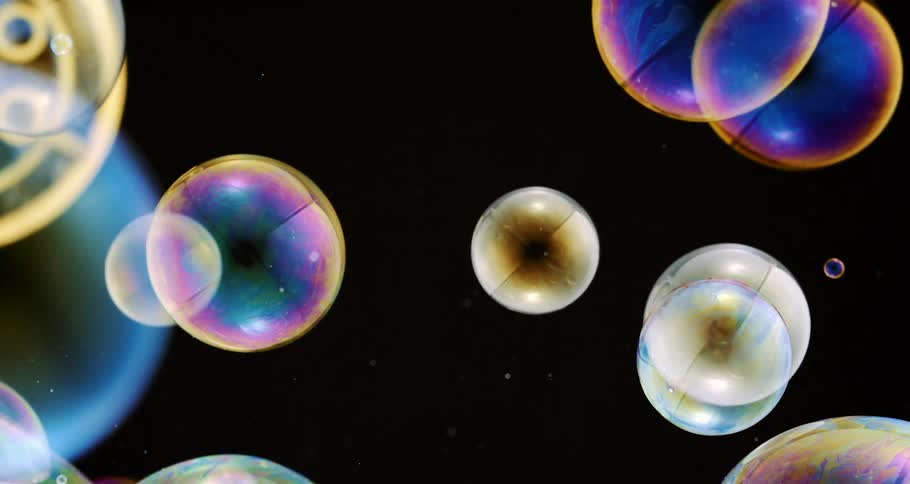 Colored bubbles bursting on a black background in slow motion