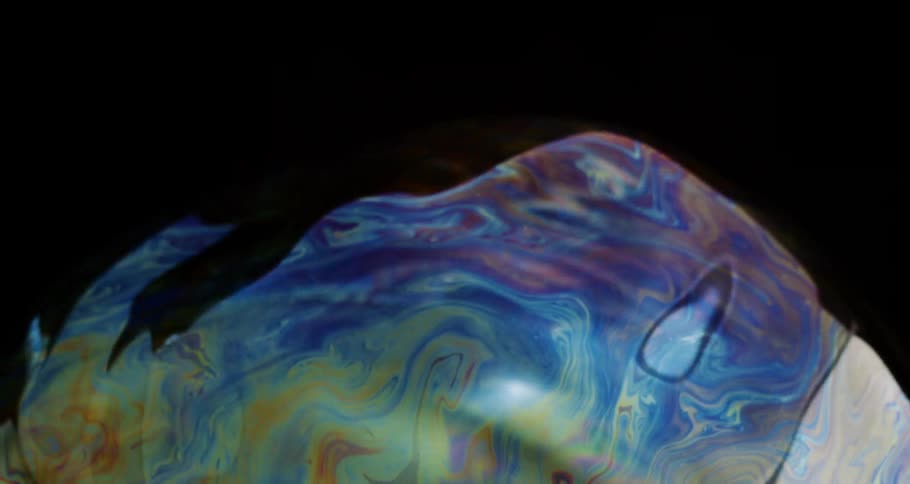 Extreme closeup of a soap bubble with abstract colorful patterns on a black background in slow motion
