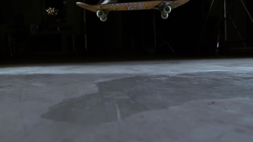 Skateboarder jumping on a skateboard in slow motion inside a dark studio room