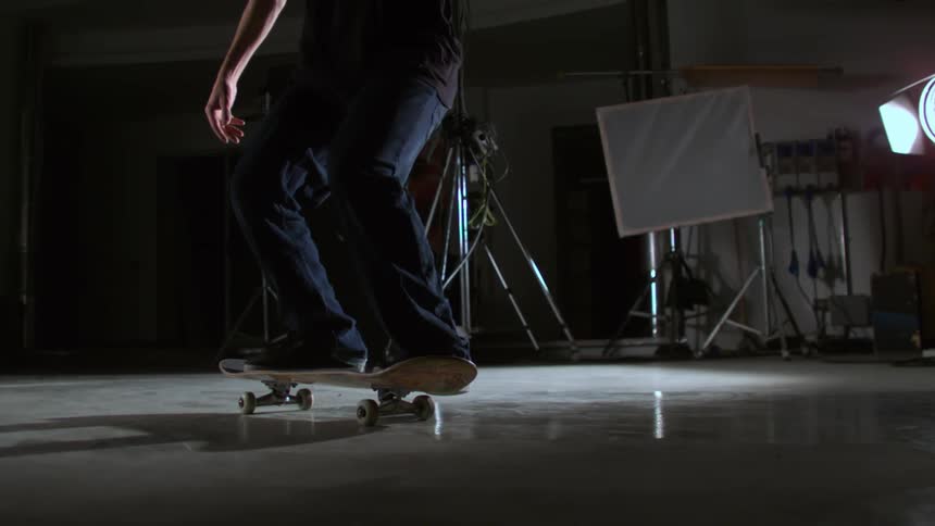 Person performing skateboard tricks inside a studio in slow motion