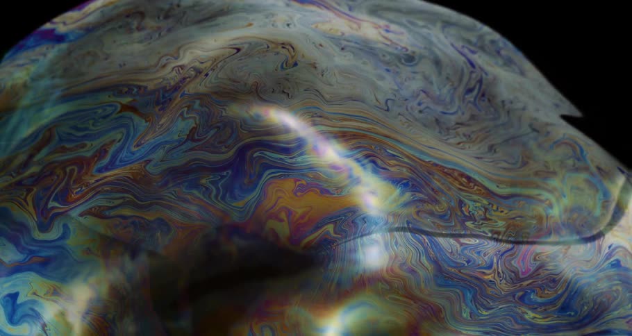 Extreme closeup of an abstract and colorful soap bubble bursting in slow motion