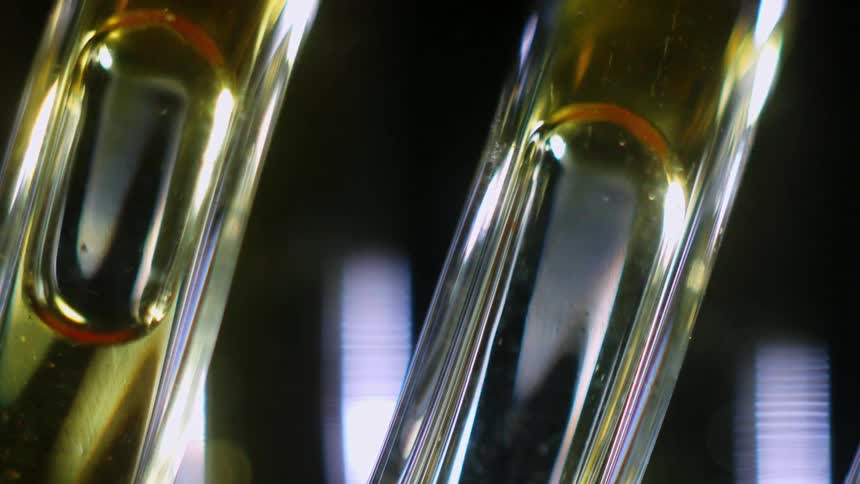 An air bubble in a honeylike liquid moves down two glass tubes that reflect a near by light