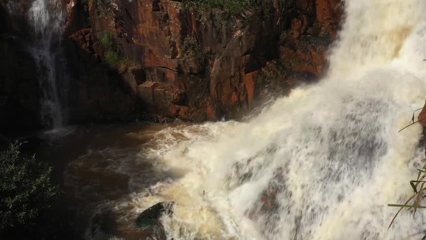 Waterfalls splash into a river along the side of a cliff
