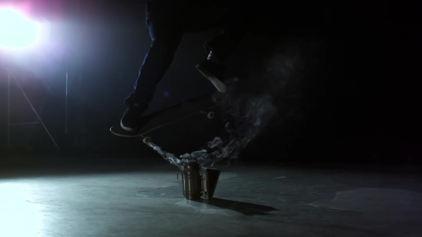 Man performs skateboard stunt in a dark room at midday
