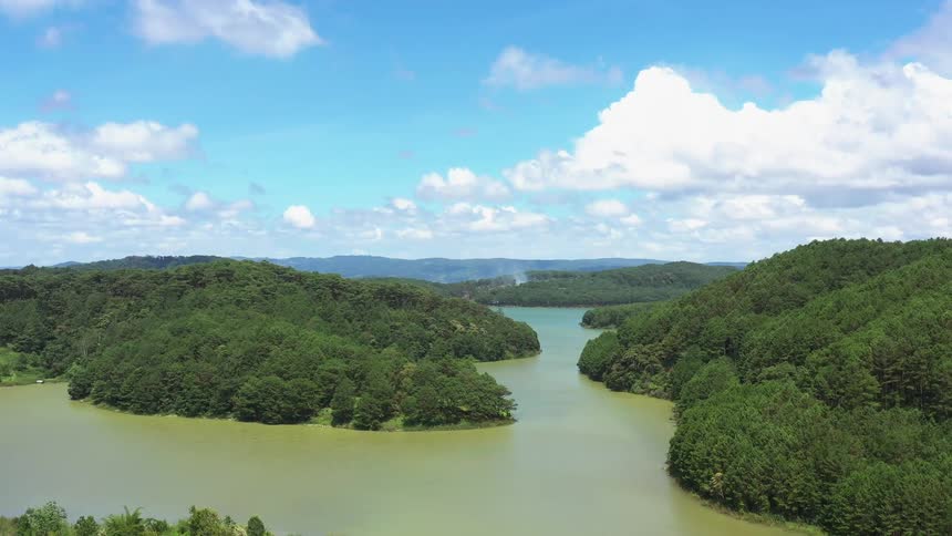 Panorama of a greenish river amidst hills with trees under a blue sky