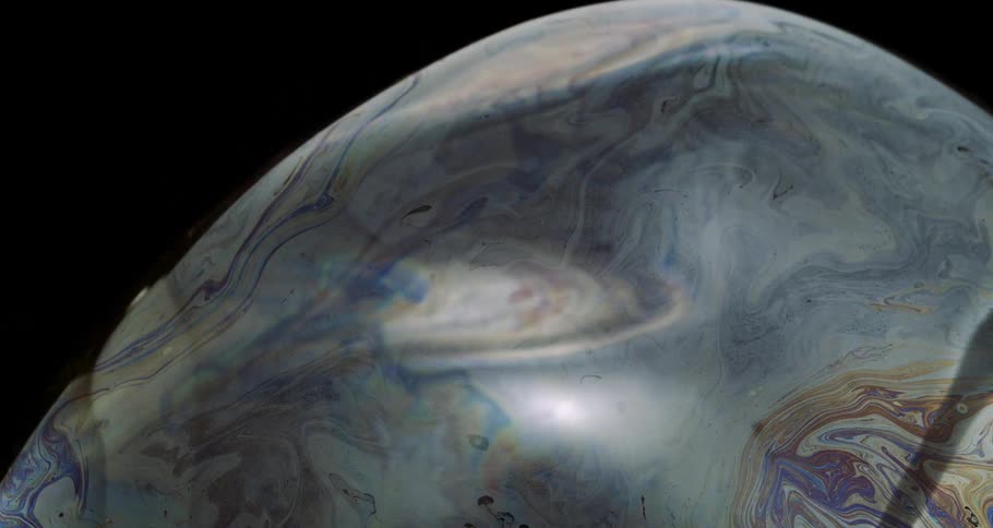 Extreme closeup of an abstract and colorful soap bubble bursting in slow motion
