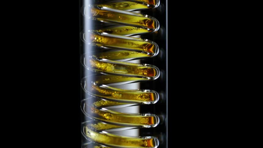 A golden liquid falling from a glass bottle in a spiral