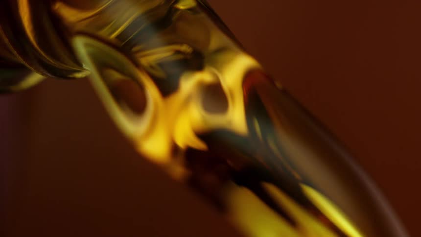 Close up of a drop of oil falling from the tip of a glass bottle