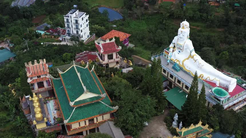 Large elaborate statue sits on roof of building complex spread over wooded lots