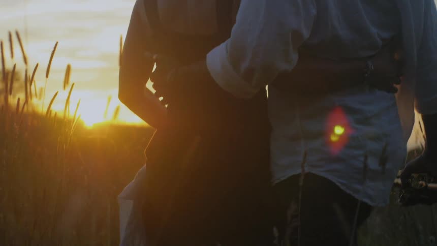 A man and woman walk through a field at sunset