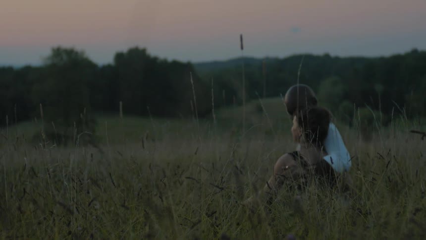 A man and woman sit in tall grass at sunset