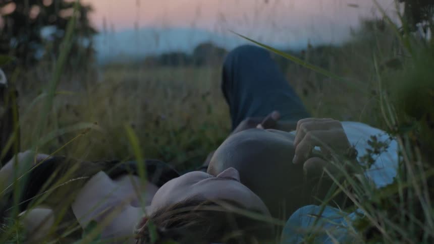 A man and woman lay down together in the grass at sunset