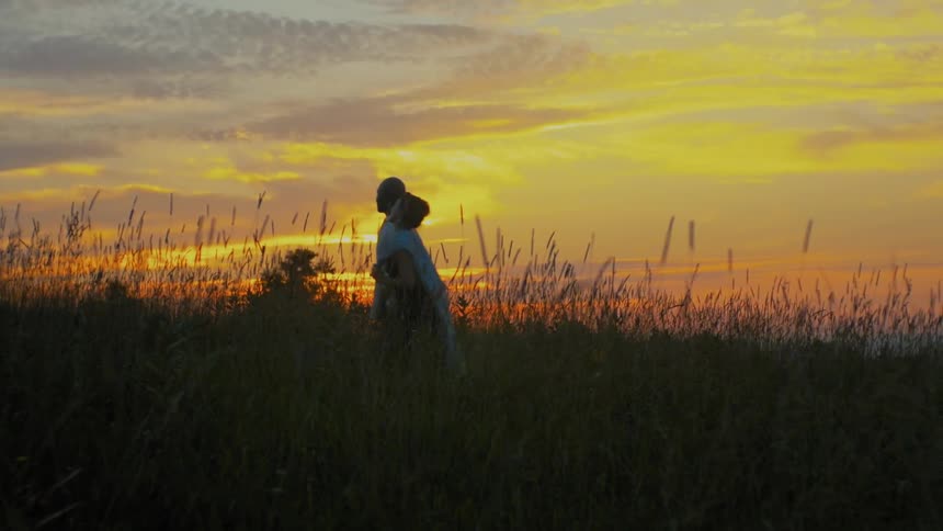 A man and woman walk in the tall grass at sunset