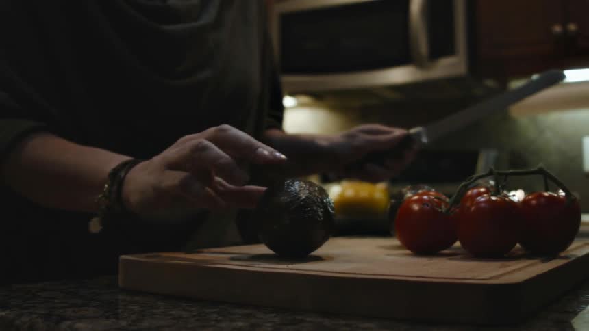 A woman picks up a knife to cut the avocado on a cutting board