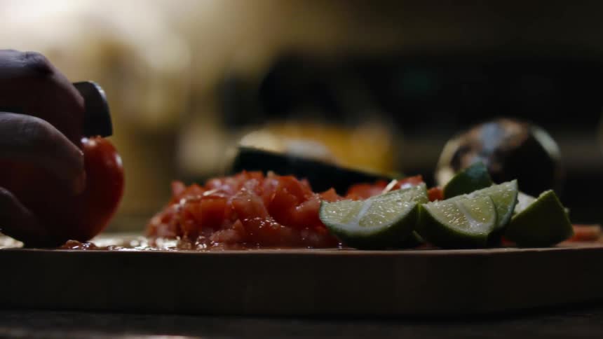 A person pushes stuff on a board to cut a tomato