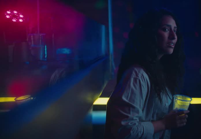 Woman holding a drink in a club looks around while standing alone