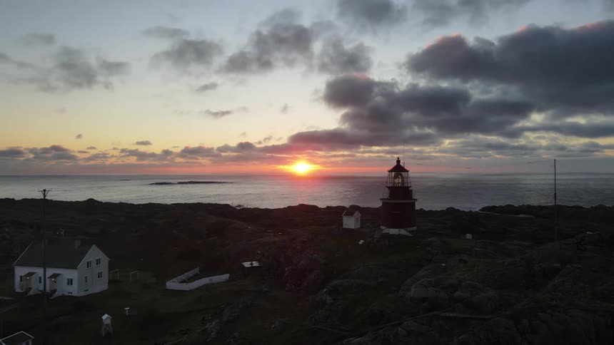 Setting sun shines across water onto beacon towering over coastal town