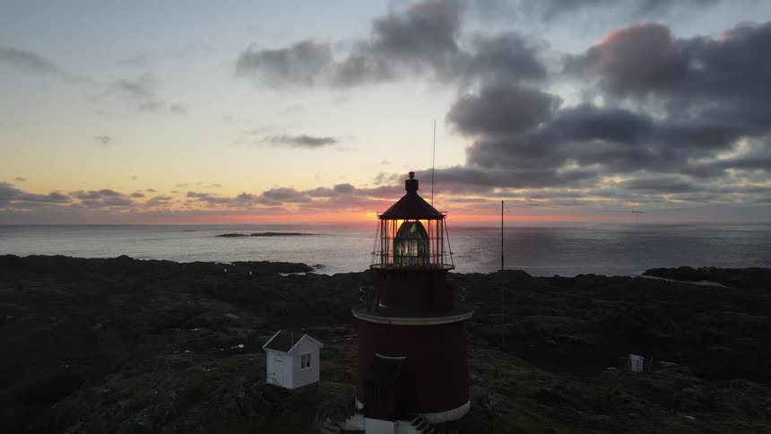 Aerial of a lighthouse on the rocky shore of the beach during sunset
