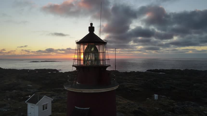 Aerial of a rocky mountain lighthouse on a beach during sunset