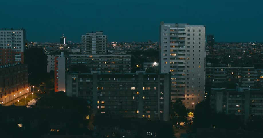 Several mediumsized buildings with lights on in a city that is at dusk