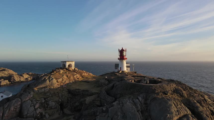 Aerial of a lighthouse on a cliff overlooking the ocean on a partly cloudy day