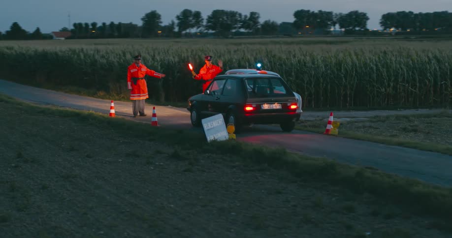 Car being stopped in a roadblock on a dirt road next to a farmland