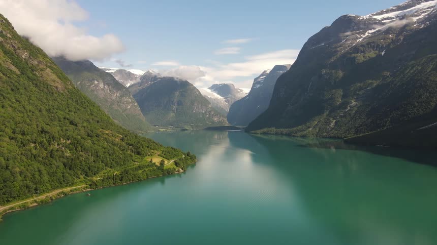 A lake reflecting a blue sky with white clouds between green mountains with fog