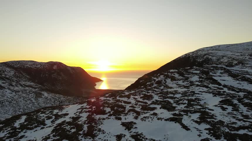 Panorama of snowcovered mountains facing the sea with the sunrise on the horizon
