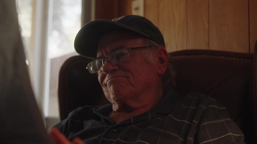 An elderly man is sitting in a chair reading the newspaper