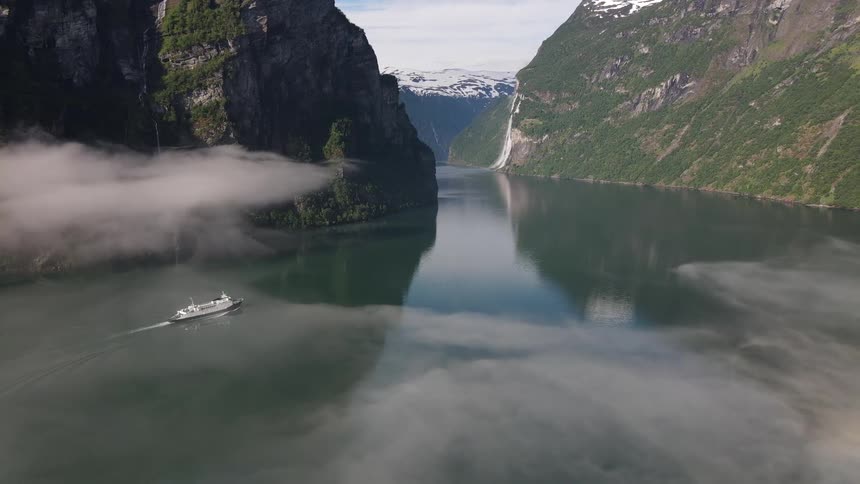A ship sailing at sea in a landscape surrounded by mountains