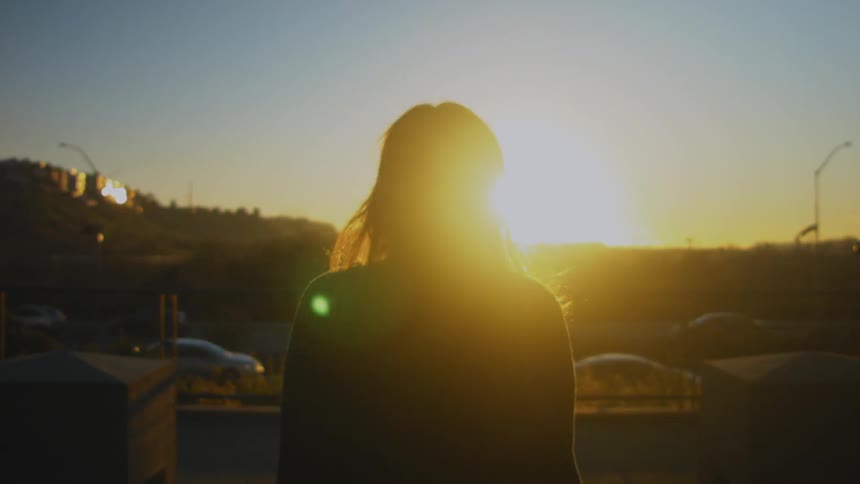 A woman walks toward a street at sunset